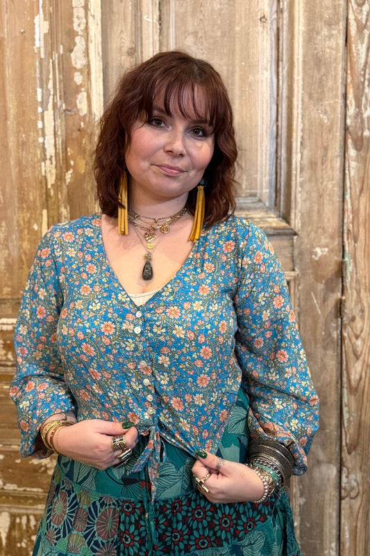 Woman wearing a floral blouse and skirt standing in front of a wooden door.