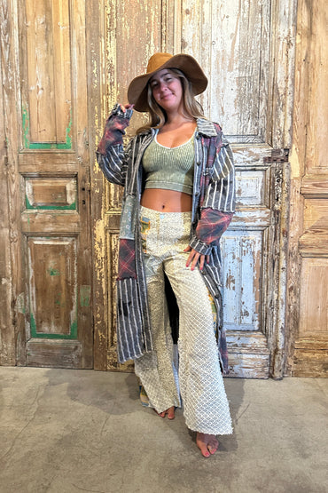 Woman posing in front of a wooden door wearing a long coat, patterned pants, and a hat.
