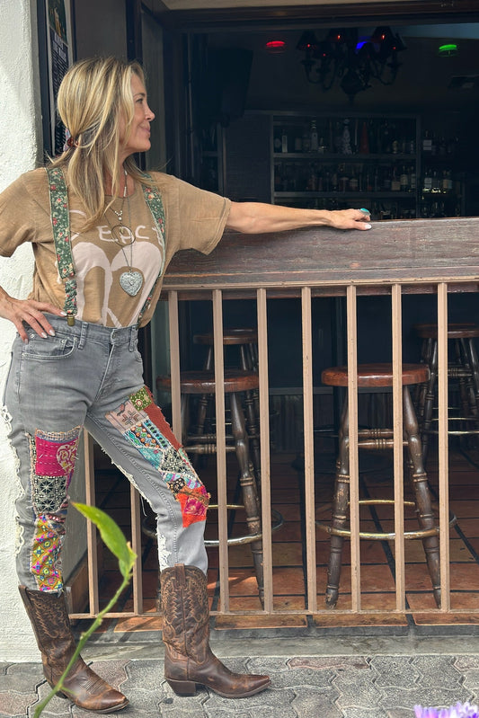 Woman standing by a bar counter wearing a graphic t-shirt, patchwork jeans, and cowboy boots.