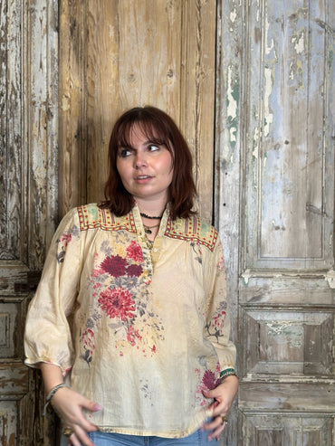 Woman wearing a floral blouse standing in front of a wooden door.