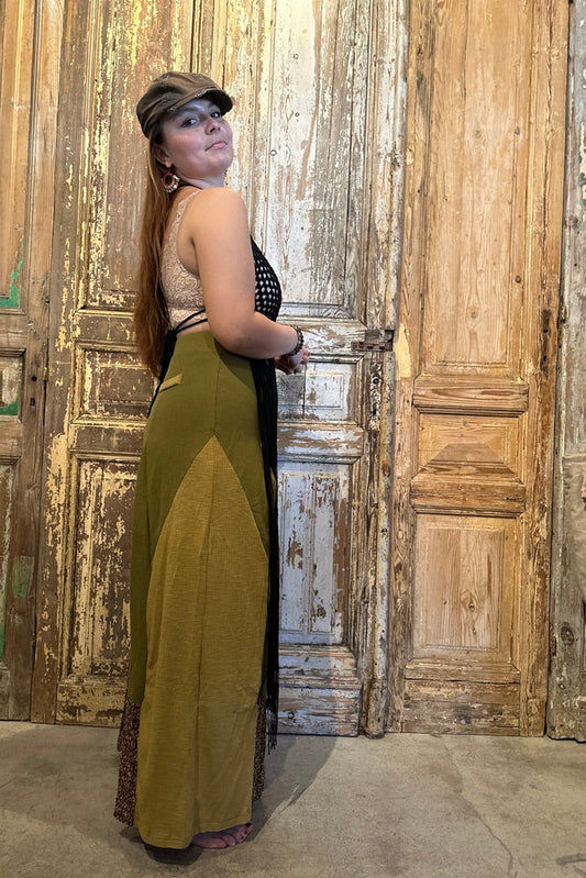 Woman in a green and black dress standing against a rustic wooden wall.