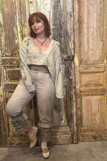 Woman in a floral top and beige pants standing in front of a rustic wooden door.