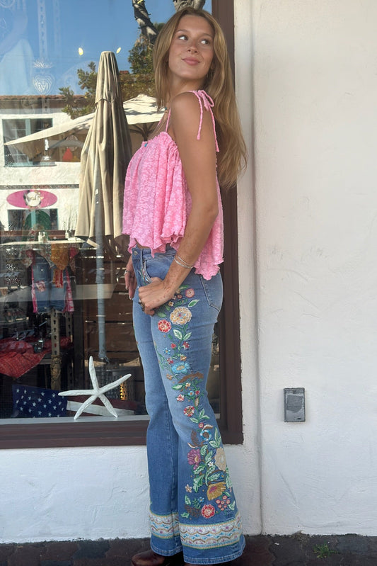 Woman wearing a pink top and floral jeans standing in front of a store window.