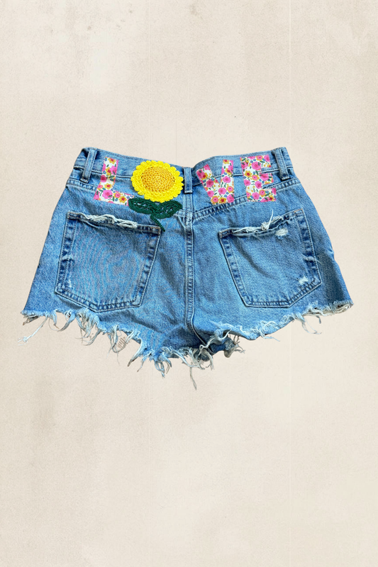 Denim shorts with floral and sunflower designs on a beige background