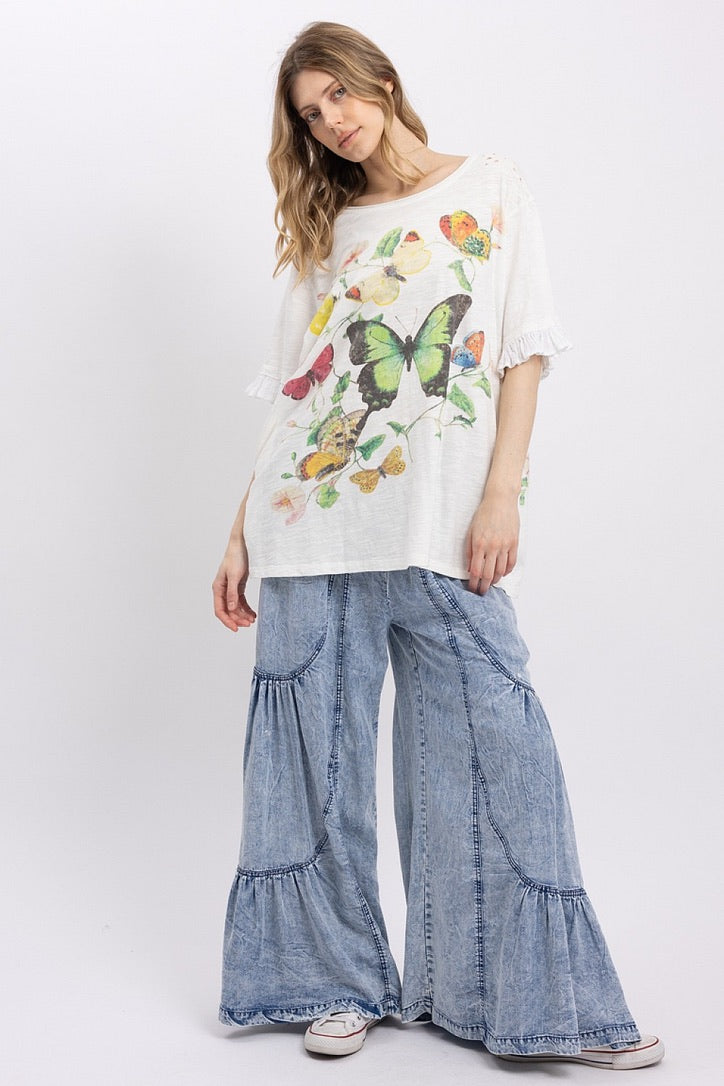 Trestles Clothing Company butterfly graphic tee with ruffled sleeves and relaxed fit worn with wide leg denim pants