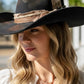 Woman wearing a black cowboy hat with a decorative band outdoors.