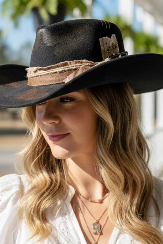 Woman wearing a black cowboy hat with a decorative band outdoors.