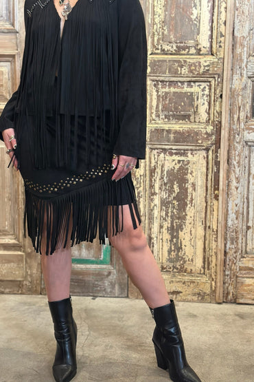 Person wearing a black fringe dress with cut-out details in front of a wooden door.