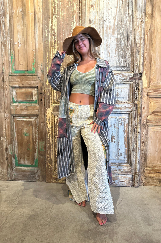 Woman posing in front of a wooden door wearing a long coat, patterned pants, and a hat.
