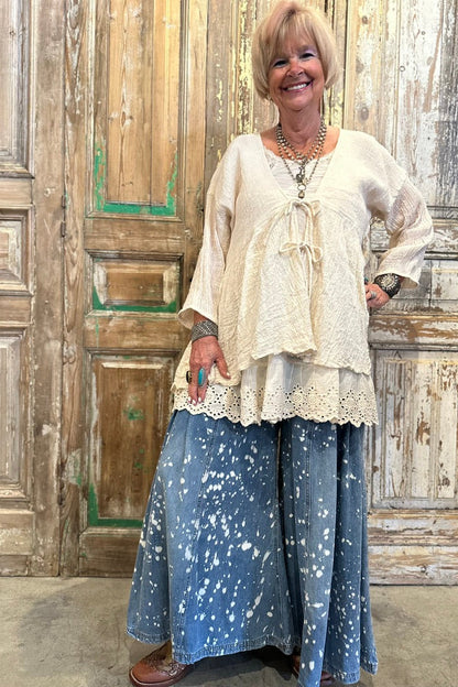 Woman wearing a white lace top and blue patterned pants standing in front of a rustic wooden door.