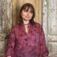 Woman wearing a patterned blouse standing in front of a wooden door.