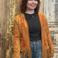 Woman wearing a brown embroidered cardigan with fringe in front of a rustic wooden door.