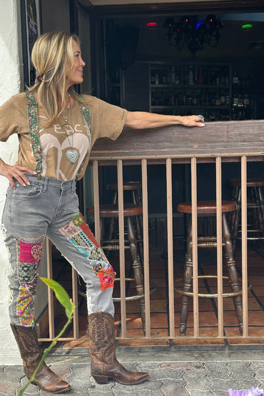 Woman standing by a bar counter wearing a graphic t-shirt, patchwork jeans, and cowboy boots.