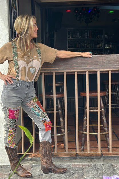 Woman standing by a bar counter wearing a graphic t-shirt, patchwork jeans, and cowboy boots.