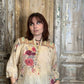 Woman wearing a floral blouse standing in front of a wooden door.