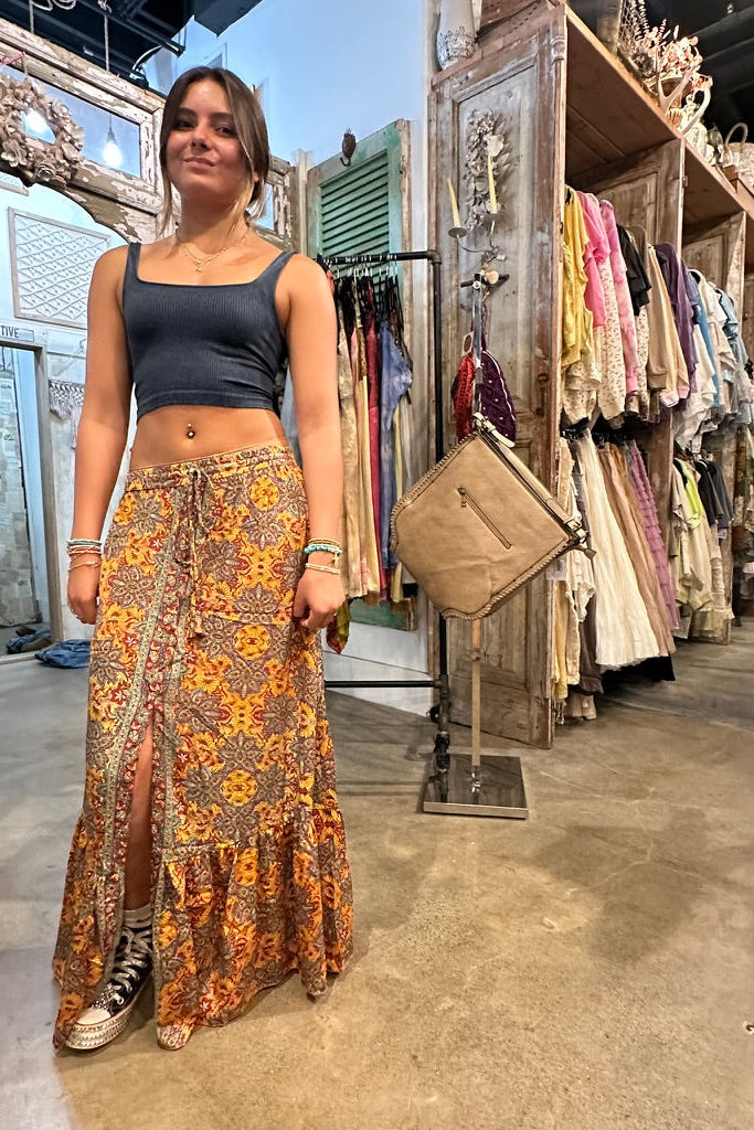 Woman in a patterned skirt standing in a clothing store with racks of clothes in the background.