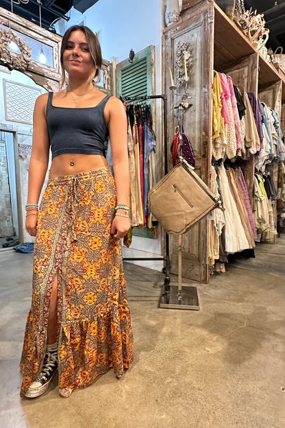Woman in a patterned skirt standing in a clothing store with racks of clothes in the background.