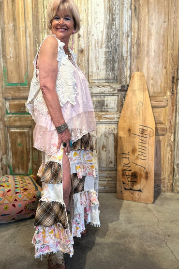 Woman in a floral dress standing next to a wooden paddle with text, against a rustic wooden wall.