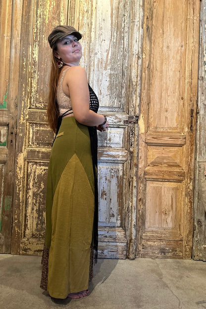 Woman in a green and black dress standing against a rustic wooden wall.