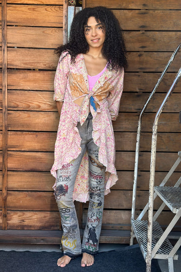 Woman wearing a floral kimono and patterned pants standing against a wooden wall.