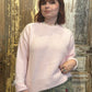 Person wearing a light pink sweater and patchwork jeans against a wooden background
