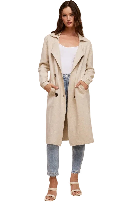 Model wearing a beige Trestles Clothing Company Beckham midi sweater coat over a white top and blue jeans