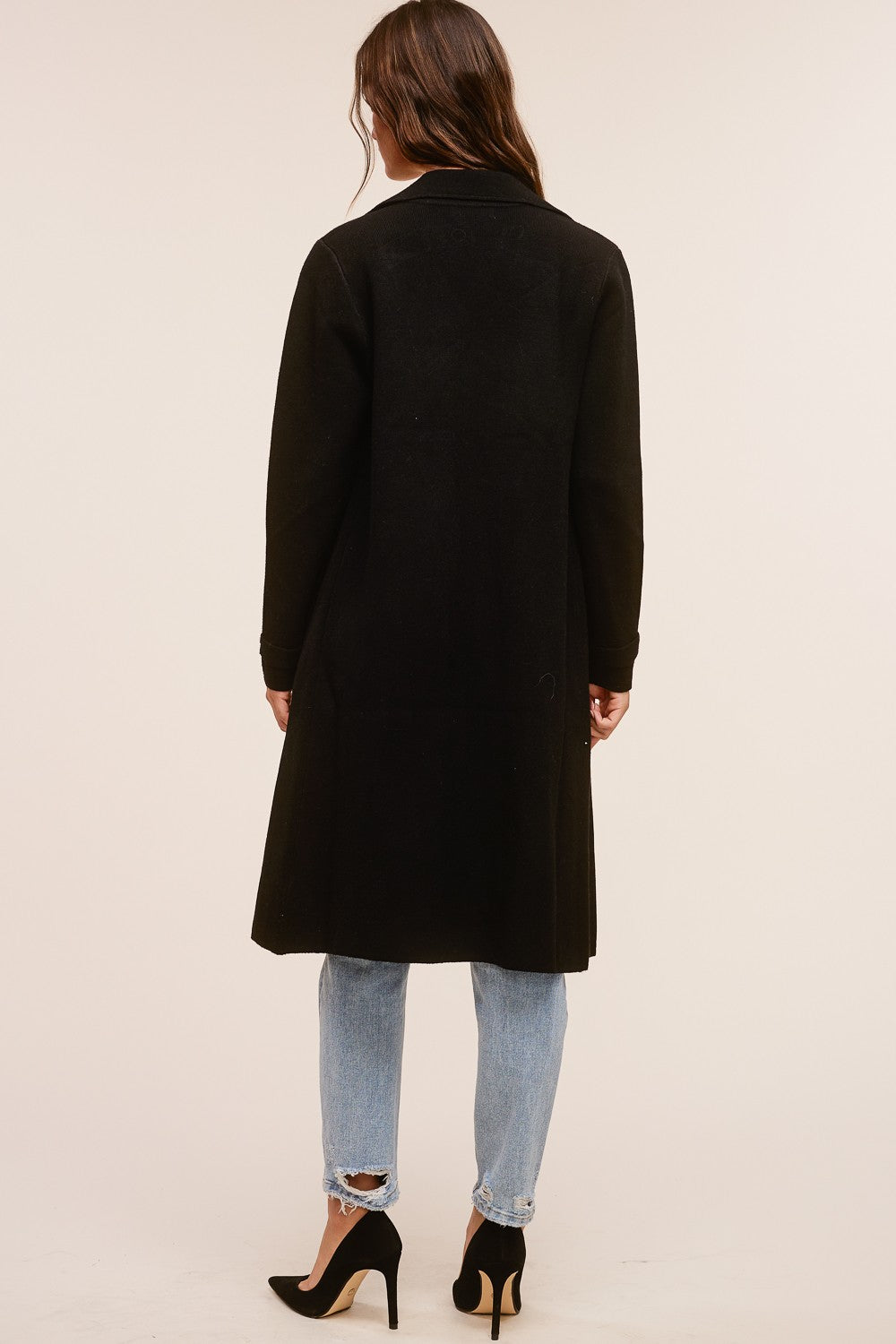 Back view of a woman wearing the black Trestles Clothing Company Beckham midi sweater coat over jeans and heels.