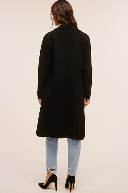 Back view of Trestles Clothing Company black midi sweater coat in a soft cashmere blend worn over jeans and heels