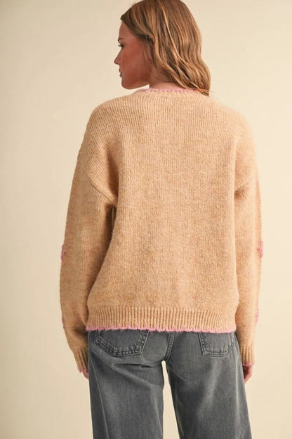 Back view of Trestles Clothing Company beige knit sweater with pink scalloped hem and floral embroidery on sleeves