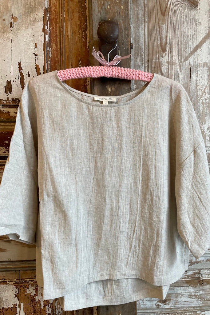 Trestles Clothing Company beige linen scoop neck top with 3/4 sleeves and a loose boxy fit on a pink hanger