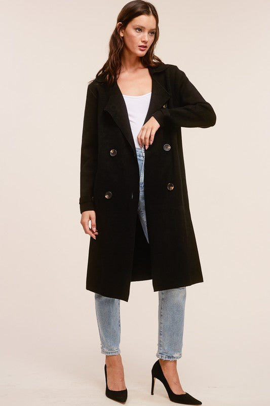 Model wearing a black Trestles Clothing Company Beckham midi sweater coat over a white top and light wash jeans