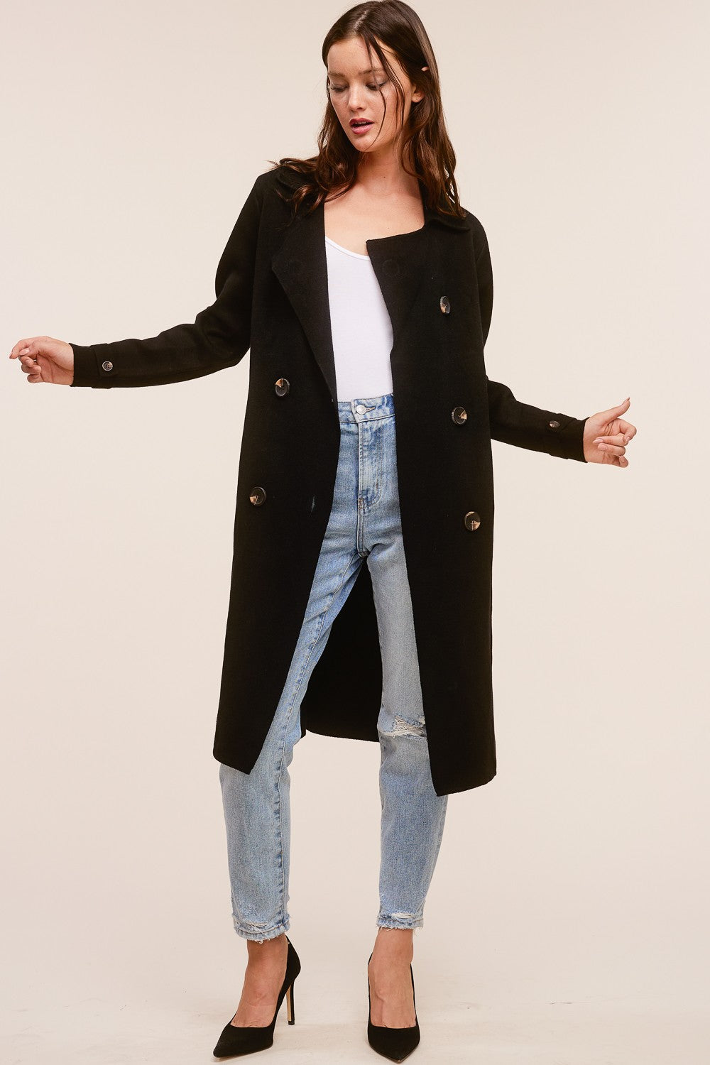 Model wearing a black Trestles Clothing Company Beckham midi sweater coat over a white top and distressed jeans.