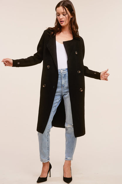 Model wearing a black Trestles Clothing Company Beckham midi sweater coat over a white top and distressed jeans.