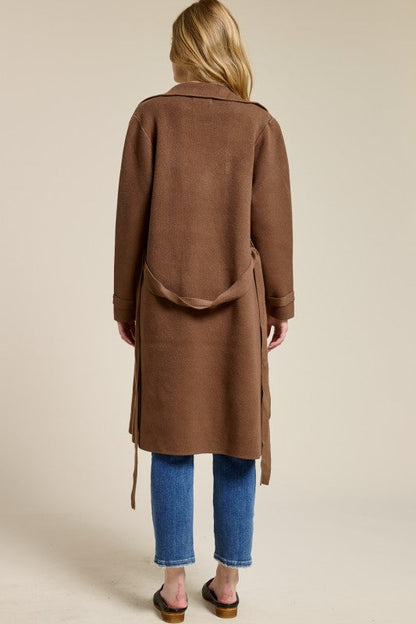 Back view of a woman wearing a brown Trestles Clothing Company midi-length cashmere blend sweater coat with a belt.