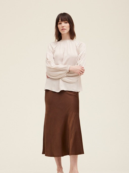 Trestles Clothing Company midi-length brown satin fit and flare skirt worn by a model with a beige long-sleeve top.