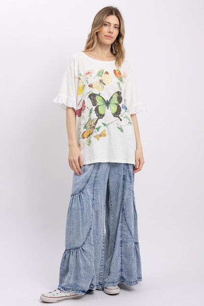 Trestles Clothing Company butterfly graphic tee with ruffled sleeves and mineral washed finish worn with denim pants