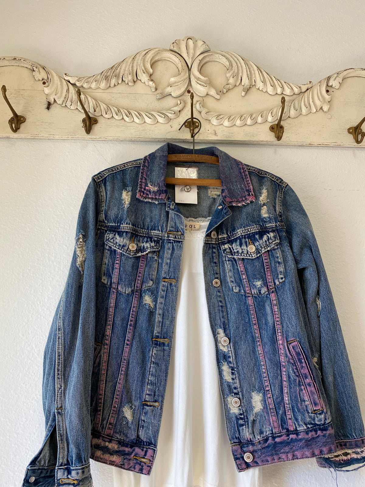 Trestles Clothing Company distressed denim jacket with hand-painted pink accents and loose fit hanging on a wall hook
