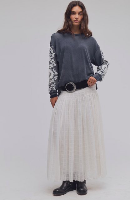 Model wearing Trestles Clothing Company Flora long sleeve tee with grey floral sleeves and a white maxi skirt