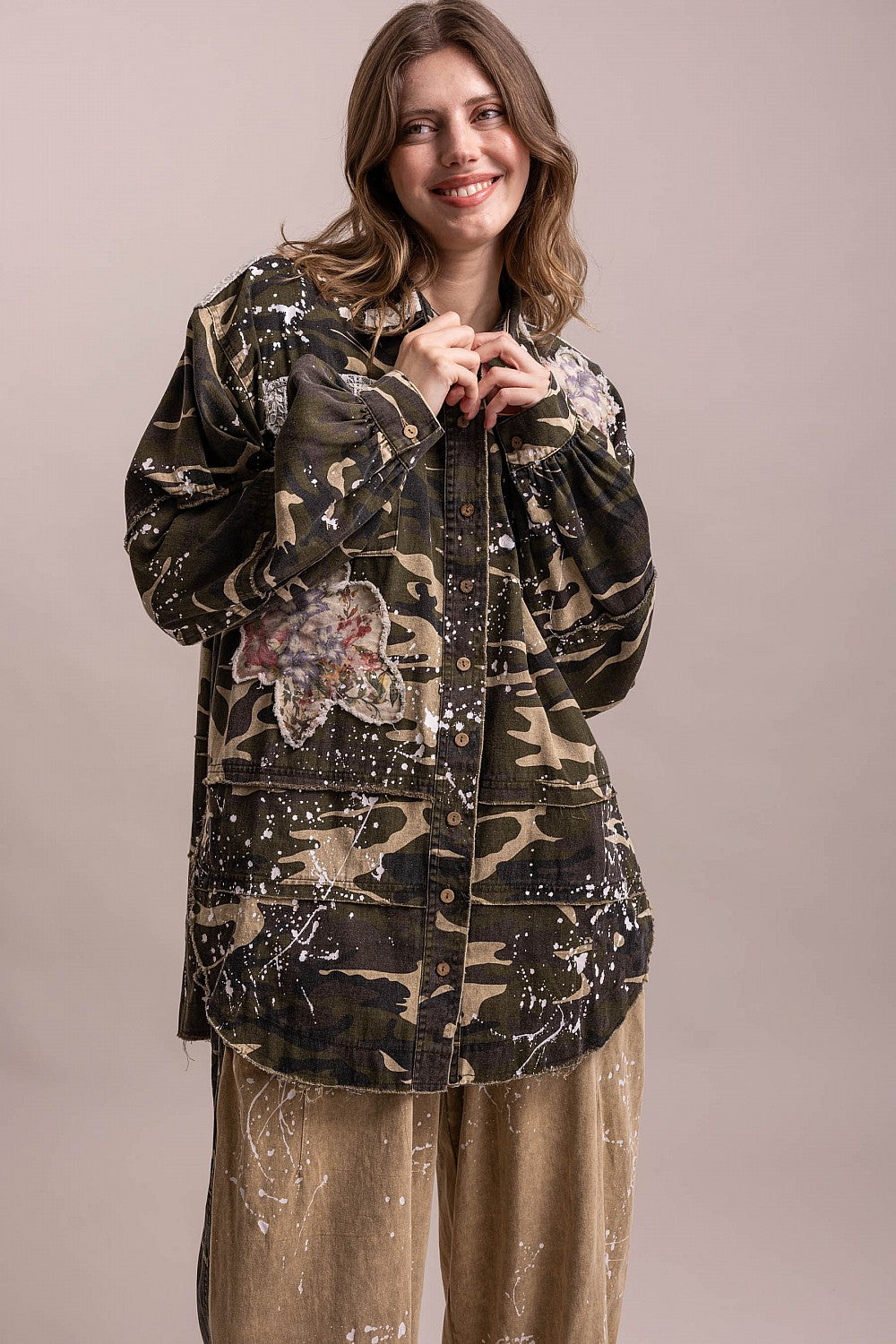 Trestles Clothing Company camo shacket with floral patches, paint splatters, and button front on a smiling model