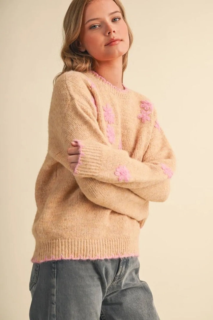 Model wearing a Trestles Clothing Company beige knit sweater with pink floral embroidery and scalloped contrast edges