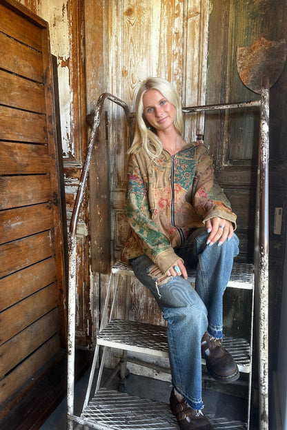 Trestles Clothing Company floral patchwork zip-up hoodie in warm autumn tones worn by a woman on rustic metal stairs.