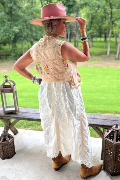 Trestles Clothing Company beige wrap vest with floral patches and lace, layered over a white lace-trimmed dress.