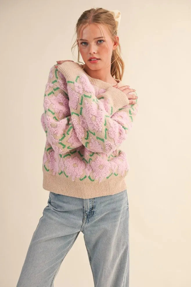 Model wearing a Trestles Clothing Company fuzzy floral knit sweater with pink flowers and beige ribbed trim.
