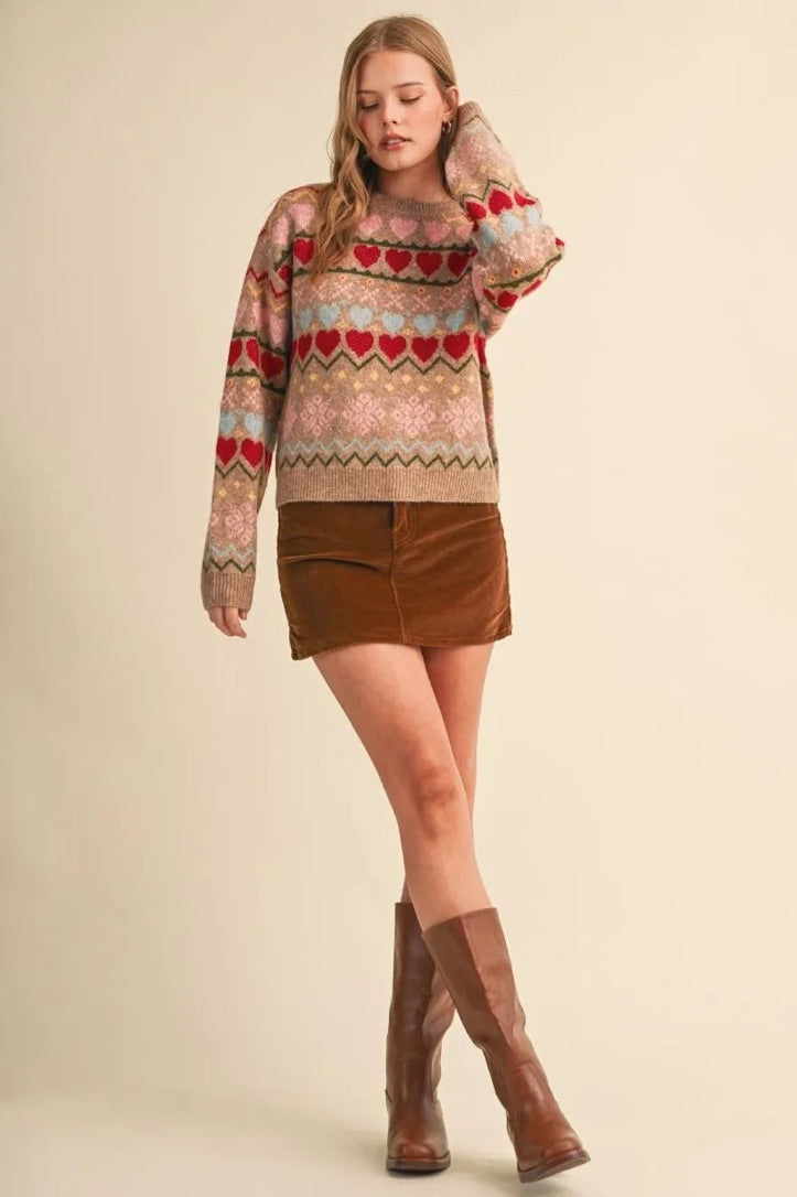 Model wearing Trestles Clothing Company gingerbread hearts sweater with geometric pattern, brown skirt, and boots