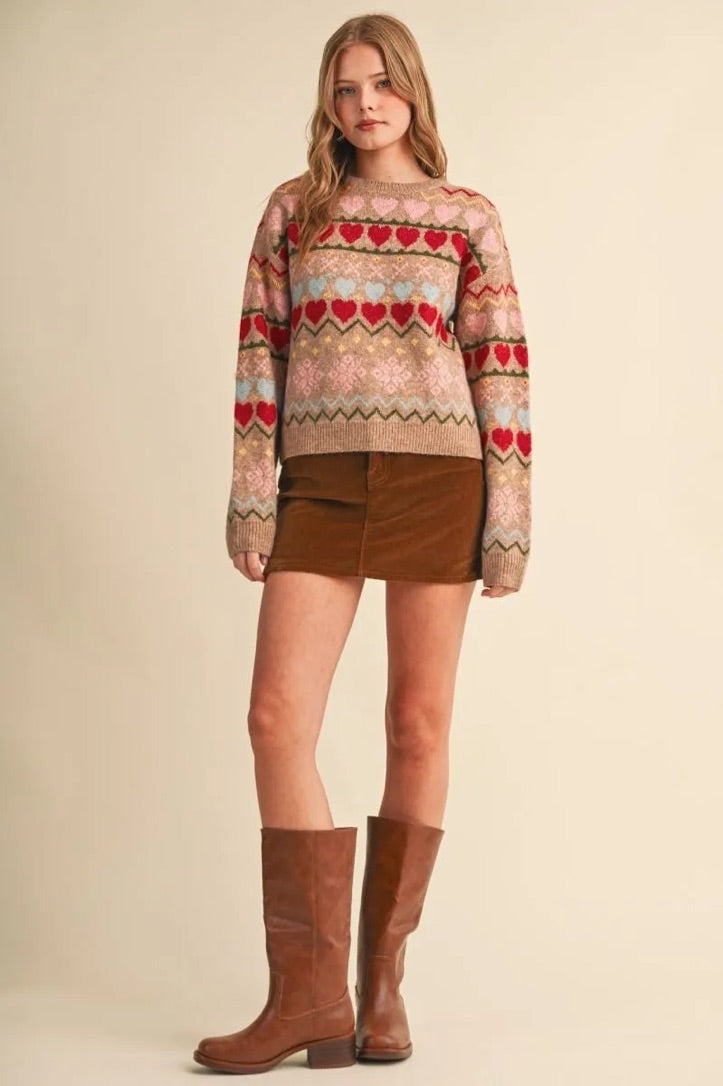 Model wearing Trestles Clothing Company gingerbread hearts sweater with geometric patterns, brown skirt, and boots.