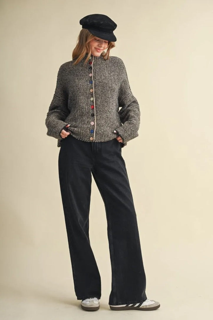 Trestles Clothing Company sweater in grey knit with mismatched colorful buttons worn with black jeans and a cap