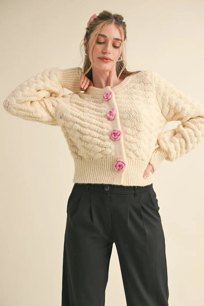 Trestles Clothing Company ivory knit cardigan with textured pattern and pink rosette buttons worn by a model