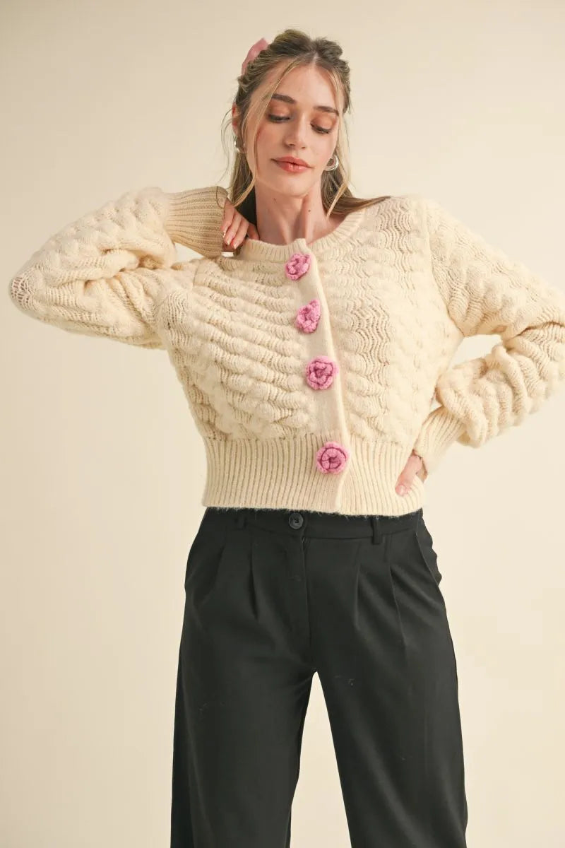 Trestles Clothing Company ivory knit cardigan with textured pattern and pink rosette buttons on a model