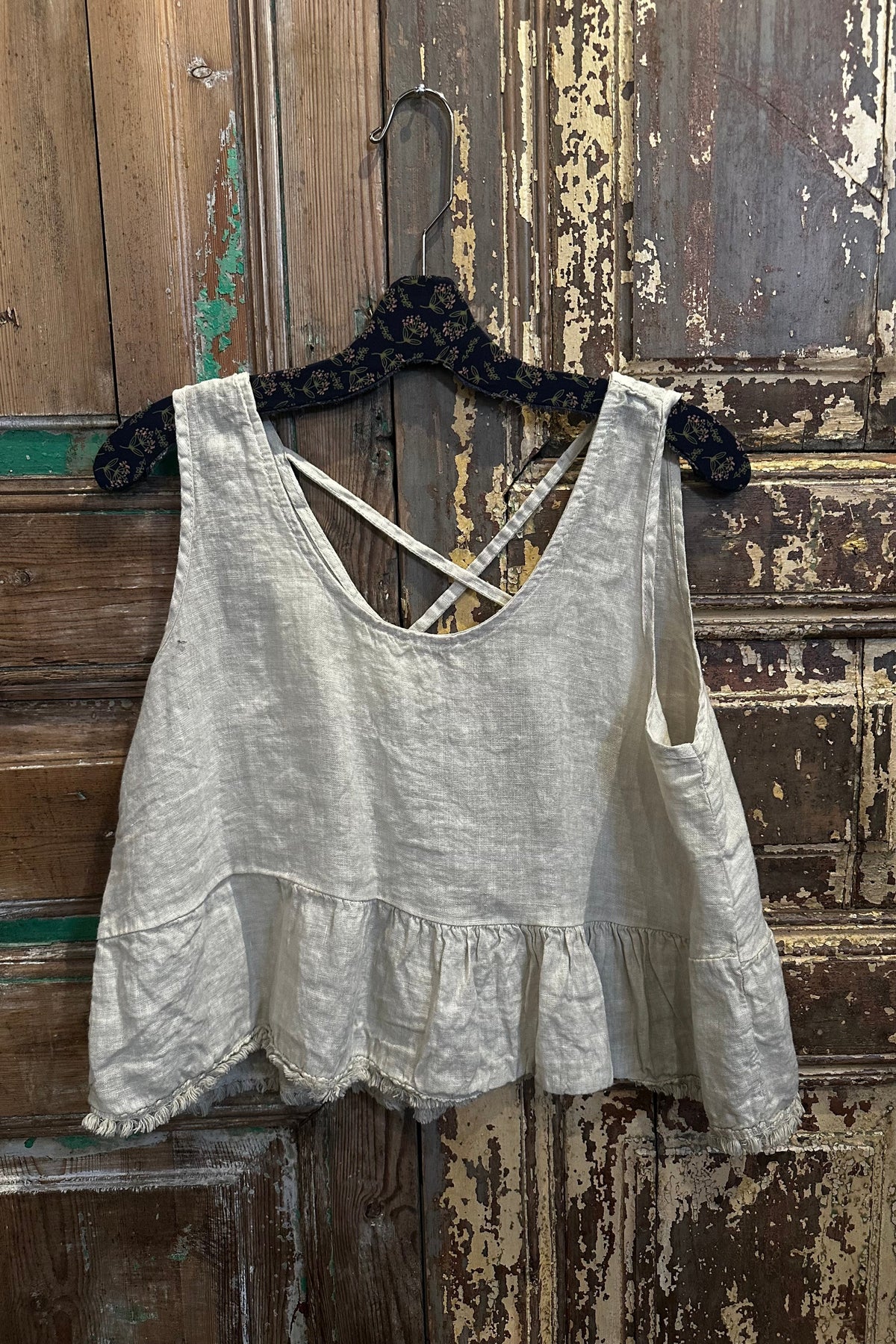 Trestles Clothing Company beige linen sleeveless top with a square neck, ruffle peplum hem, and criss-cross back detail.
