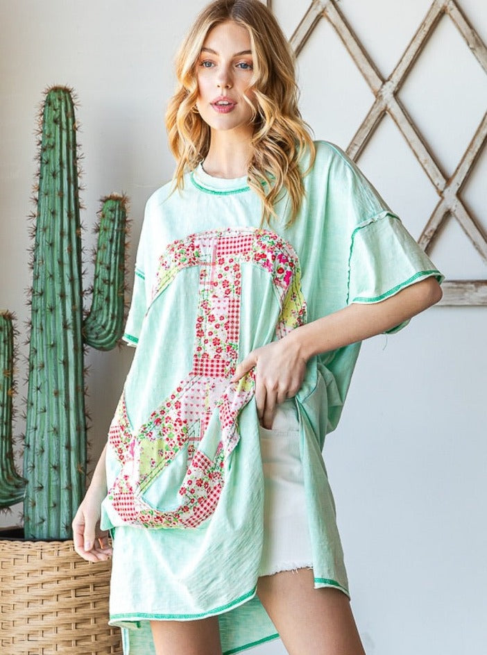 Trestles Clothing Company oversized mint green knit tee with a floral applique peace sign, worn as a beach cover up.